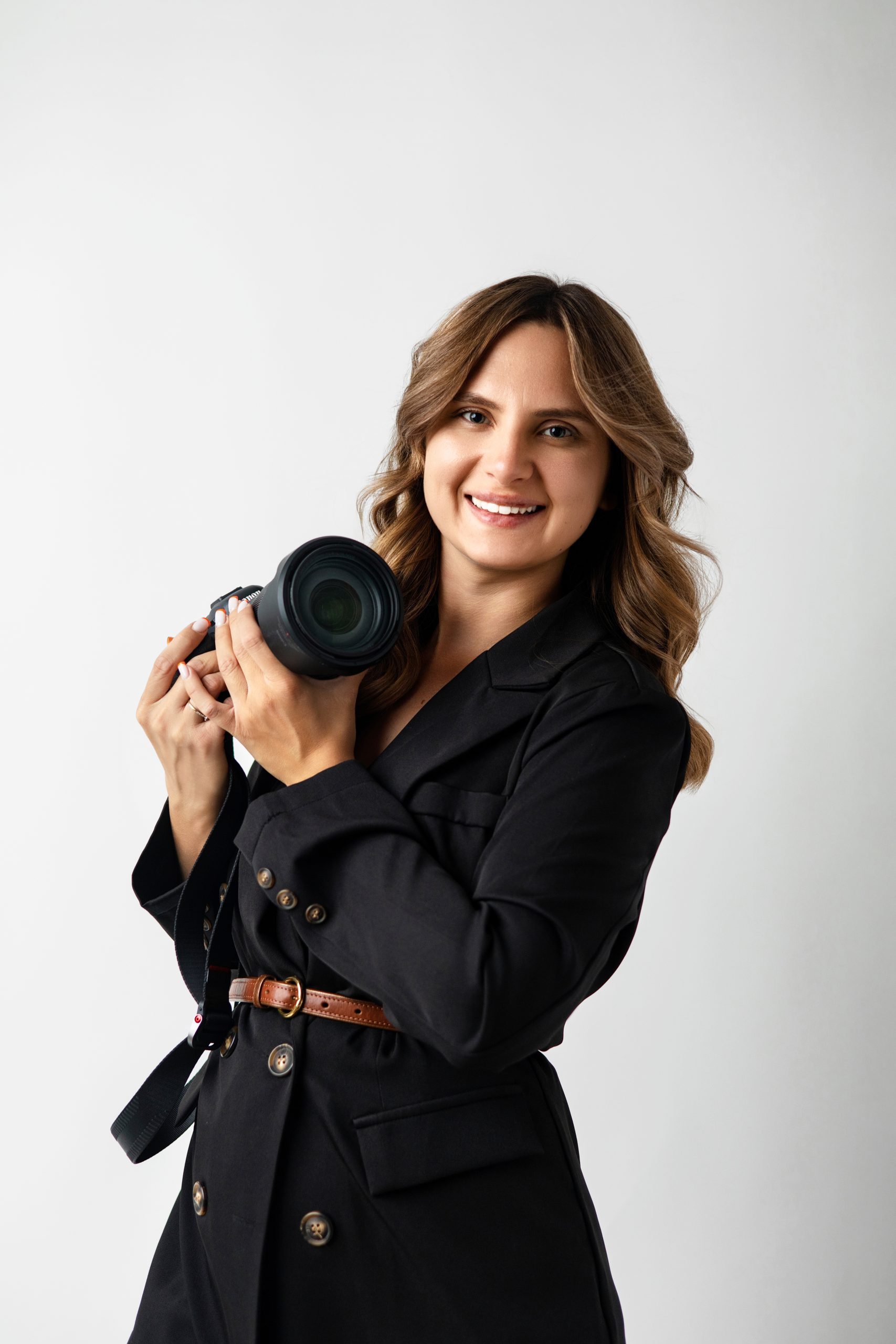 Uśmiechnięty portret kobiety, która trzyma aparat fotograficzny i ma na sobie czarną marynarkę.